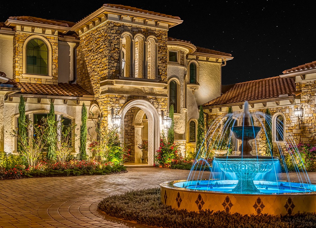 Warm landscape lighting on a stone facade, cypress trees and lit fountain