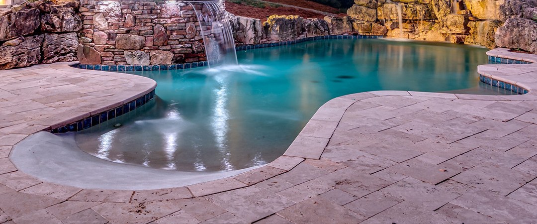 Pool and rock waterfall glowing under evening landscape lighting